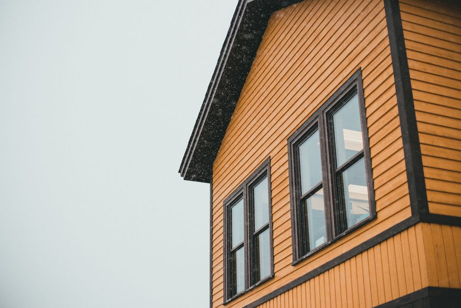 Yellow wood-sided house with dark-framed windows under an overcast sky