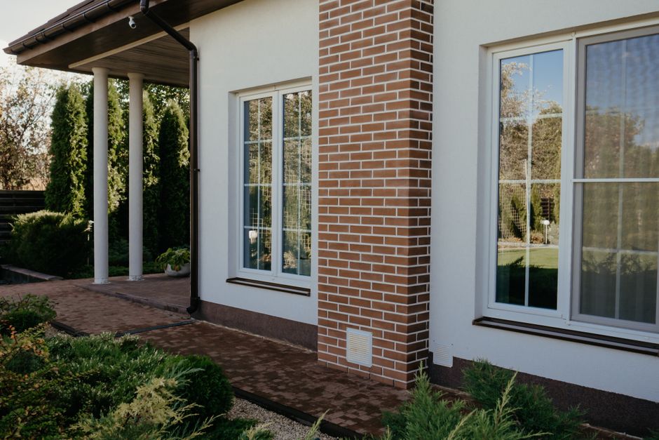 White stucco house with tall white-framed windows beside a brick pillar and a garden path