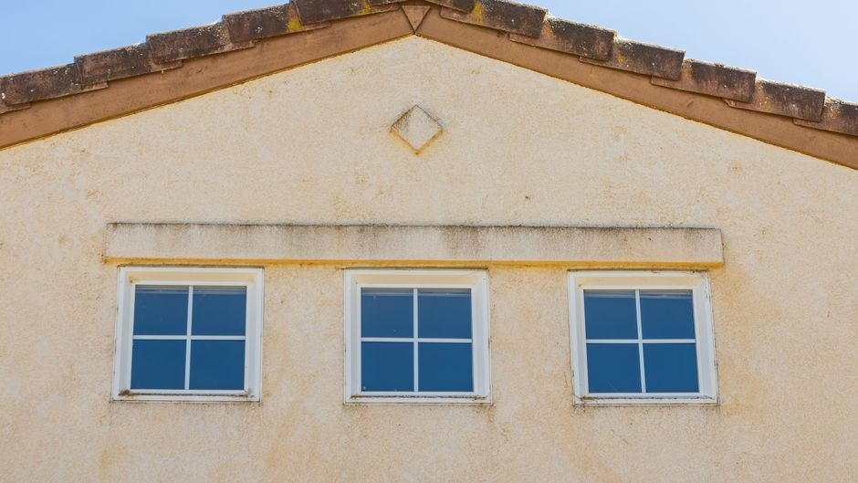 Three small white-framed windows set in a pale stucco gable under a tile roof edge