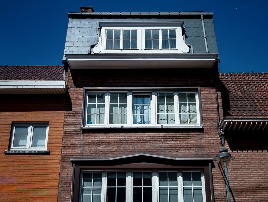 Brick house front with white-framed windows on three floors and a dormer under a blue sky