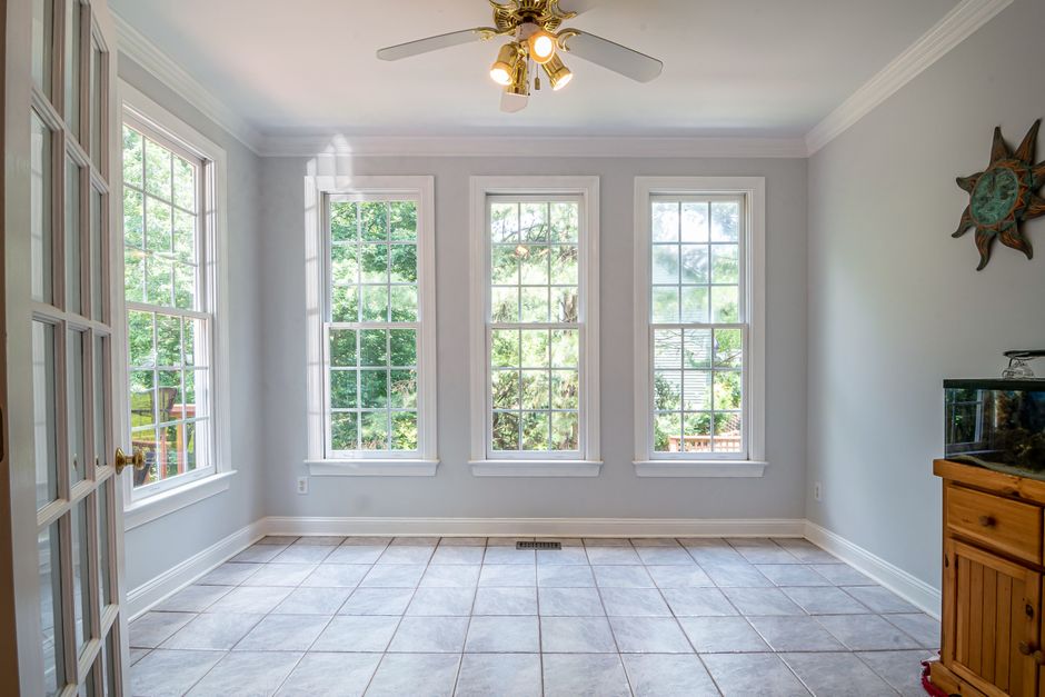 Empty room with three tall white double hung windows, tile floor and a ceiling fan
