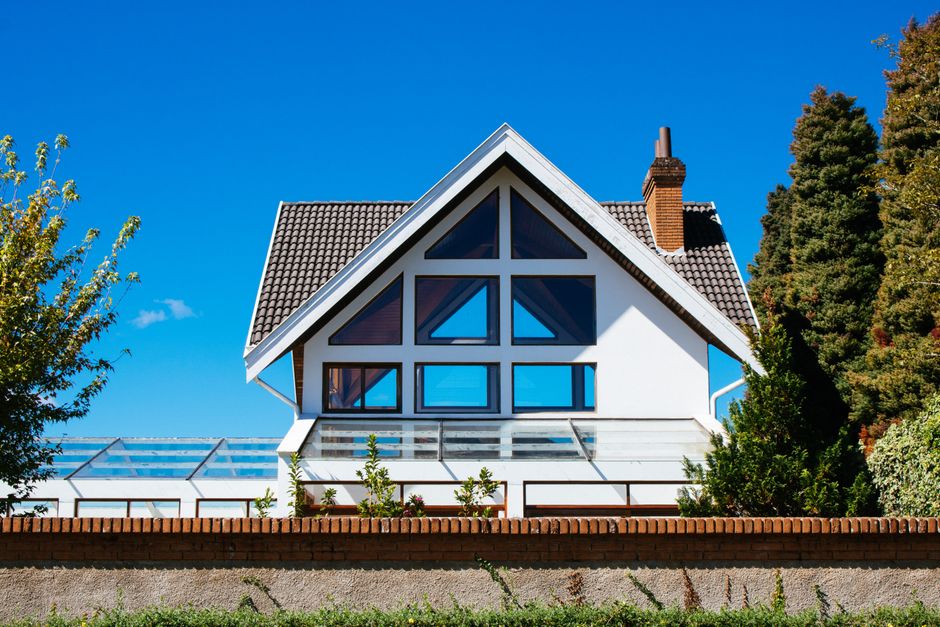 White house with a large triangular gable window under a blue sky behind a brick wall