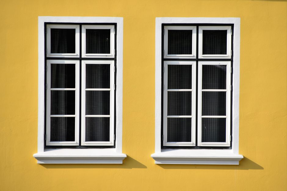 Two white-framed windows with dark glass set in a bright yellow wall