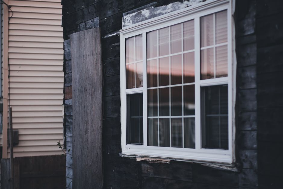 White-framed window with trim paint peeling on a dark wood wall at dusk