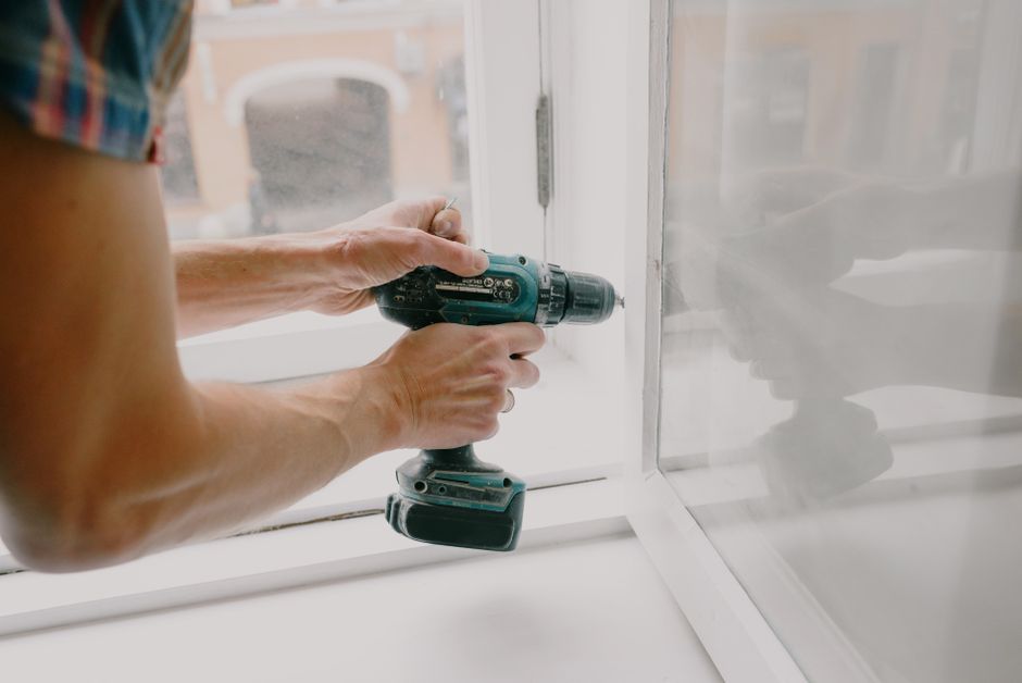 Person using a cordless drill on a white window frame inside a room