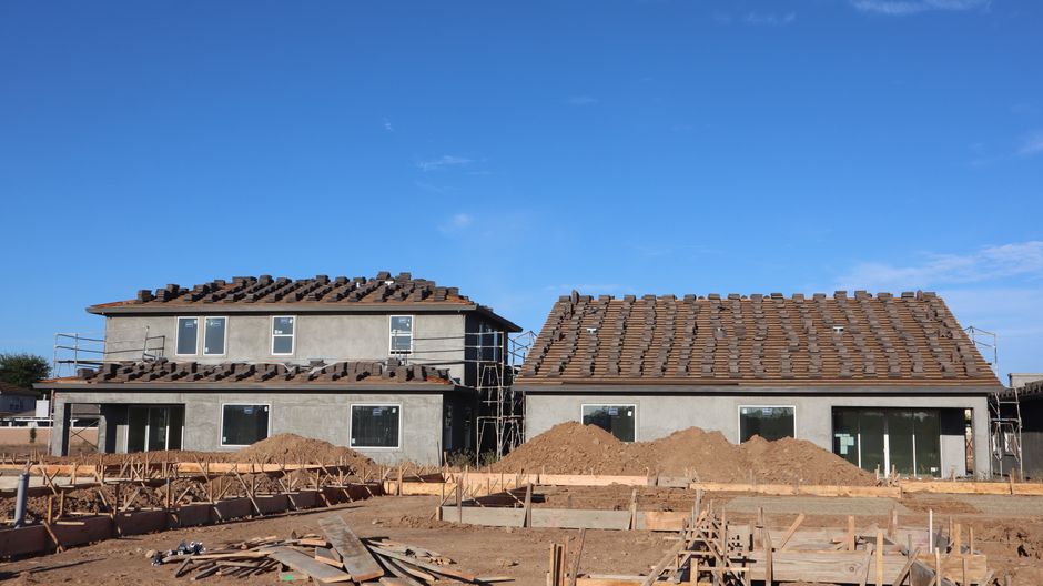Two stucco buildings with scaffolding and new roof tiles above a dirt lot