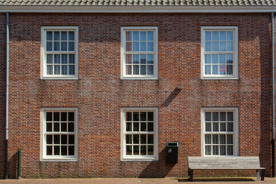 Brick building front with six white-framed multi-pane windows and a bench on the pavement