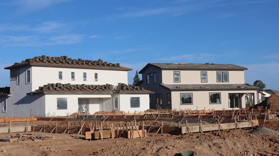 Two stucco houses under construction with roof tiles stacked on the roofs and window openings below